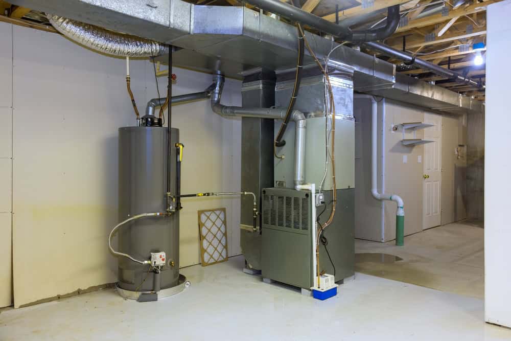 A clean basement with exposed beams and a cement floor features a water heater and HVAC unit. Ductwork extends across the ceiling. There's a white door on the back wall and a few pipes running along the walls.